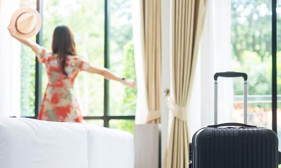 Reisende mit Trolley bezieht elegantes Hotelzimmer mit Aussicht in den Park | © Gettyimages.com/Panuwat Dangsungnoen
