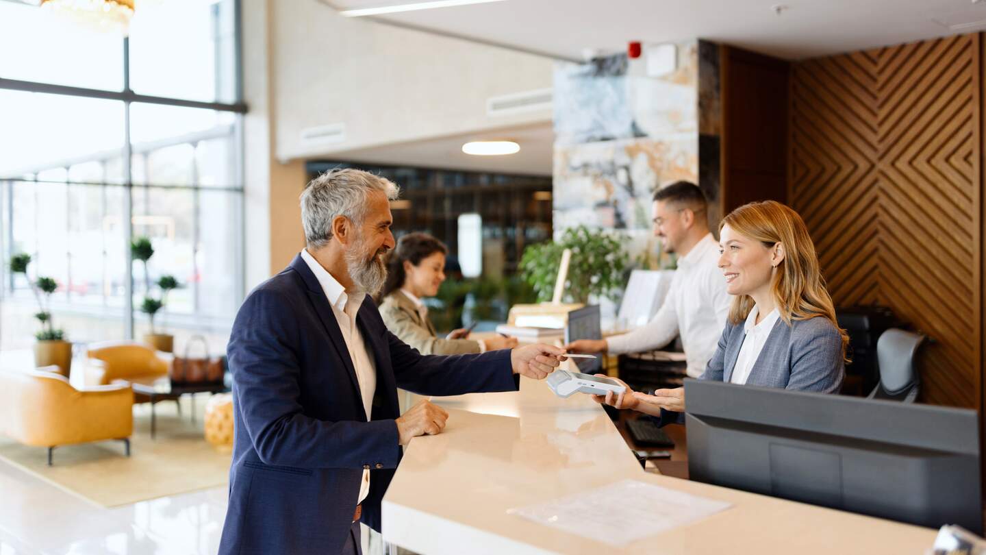 Mann an der Rezeption eines Hotels | © gettyimages.com/Anchivy