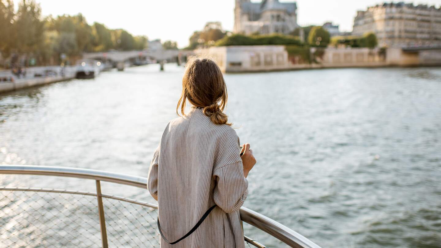 Frau genießt den Landschaftsblick auf die Stadt Paris vom Boot aus | © Gettyimages.com/RossHelen