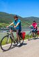 Drei Radfahrer im Sommer neben dem Fluss, im Hintergrund ein Flusskreuzfahrtschiff | © Carina Eßbüchl