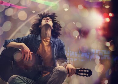 Junger Mann spielt Gitarre vor kuenstlerischem Hintergrund | © Gettyimages.com/seb_ra 