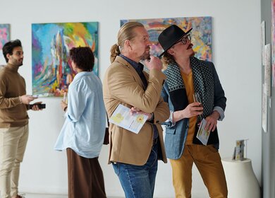 Menschen betrachten Gemaelde an der Wand und diskutieren darueber, waehrend sie die Ausstellung moderner Kunst in der Galerie besuchen | © Gettyimages.com/shironosov
