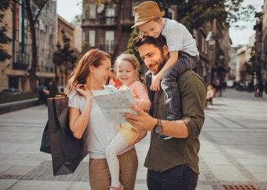 Familie, bestehens aus Mutter, Vater, Sohn und Tochter, gehen in der Stadt spazieren. Mutter trägt Tochter auf dem Arm, Sohn sitzt bei Vater auf den Schultern. | © Gettyimages.com/Geber86