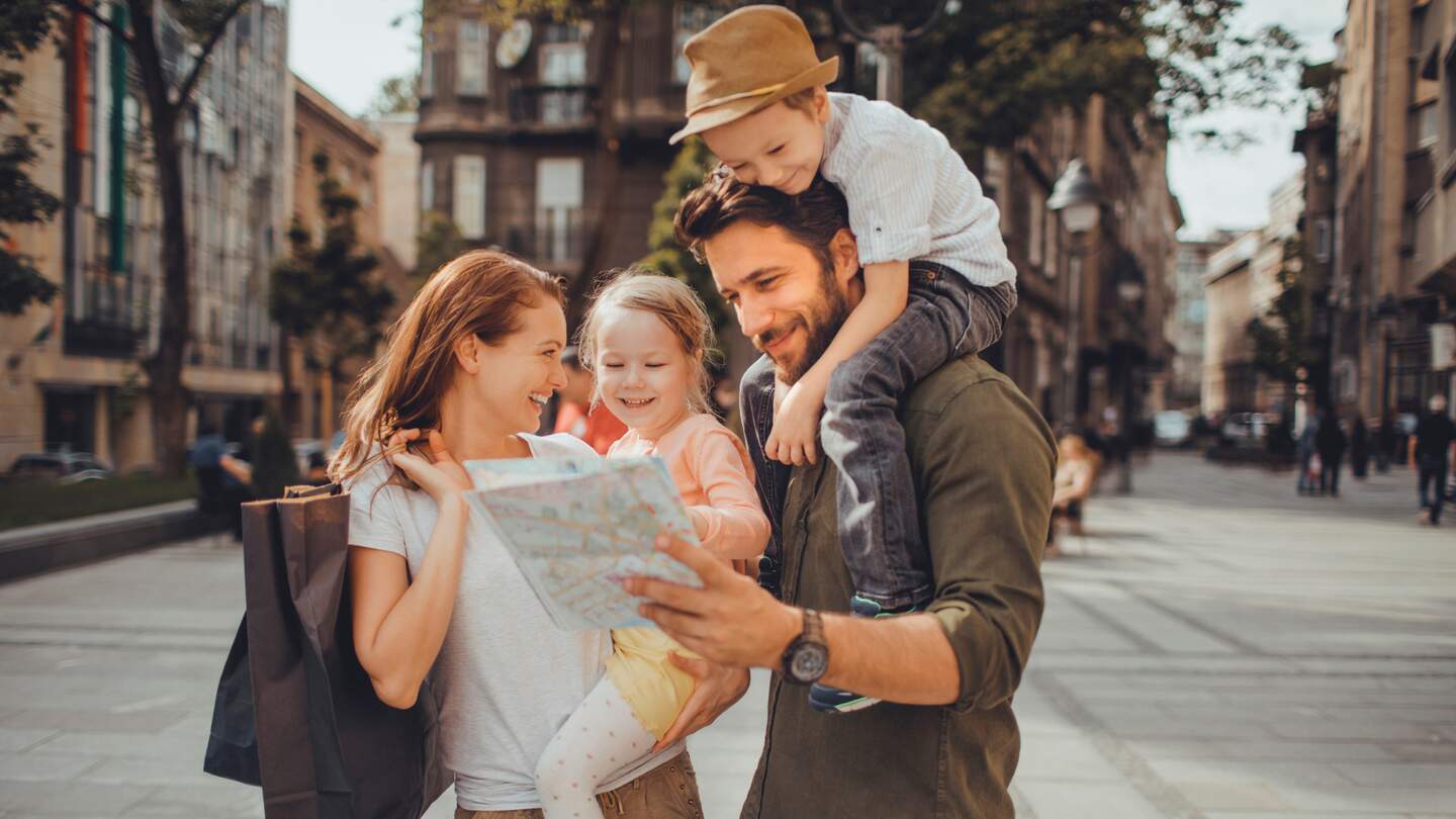 Familie, bestehens aus Mutter, Vater, Sohn und Tochter, gehen in der Stadt spazieren. Mutter trägt Tochter auf dem Arm, Sohn sitzt bei Vater auf den Schultern. | © Gettyimages.com/Geber86