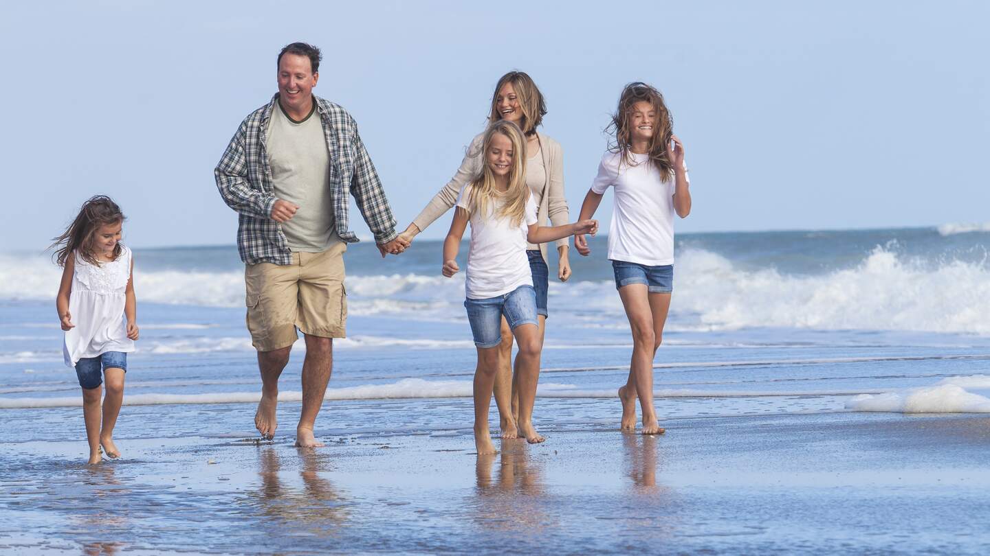 Eltern gehen mit ihren drei Toechtern am Strand spazieren | © Gettyimages.com/Spotmatik