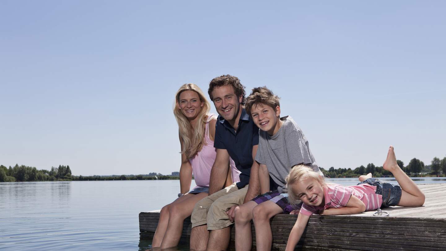 Familie sitzt auf einem Steg und laesst die Fuesse in den See haengen | © Gettyimages.com/Johnny Valley