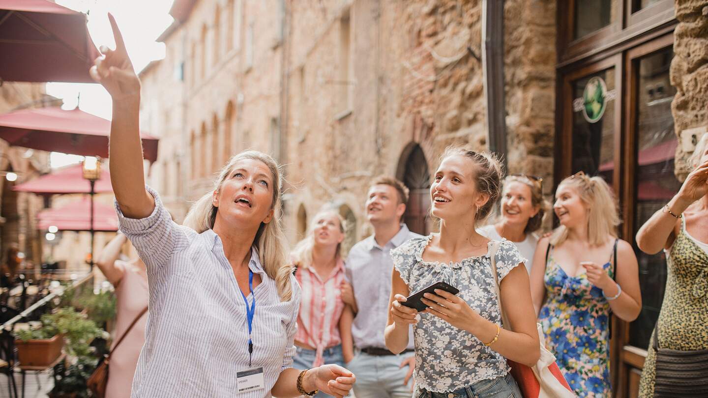 Kleine Reisegruppe auf historischem Stadtrundgang. Sie hoert einem Reiseleiter zu, der ueber die Architektur und die Geschichte spricht. | © Gettyimages.com/SolStock