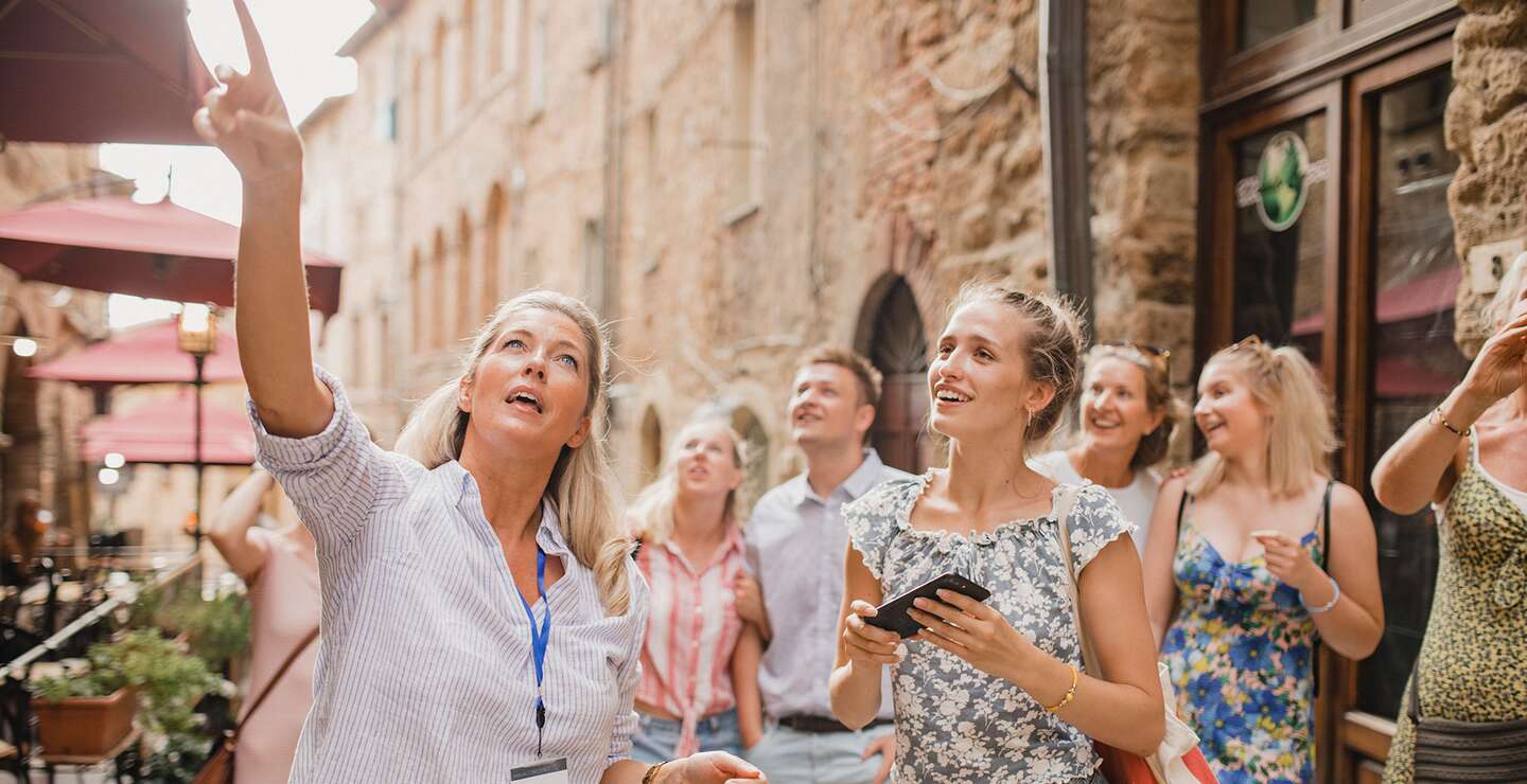 Kleine Reisegruppe auf historischem Stadtrundgang. Sie hoert einem Reiseleiter zu, der ueber die Architektur und die Geschichte spricht. | © Gettyimages.com/SolStock