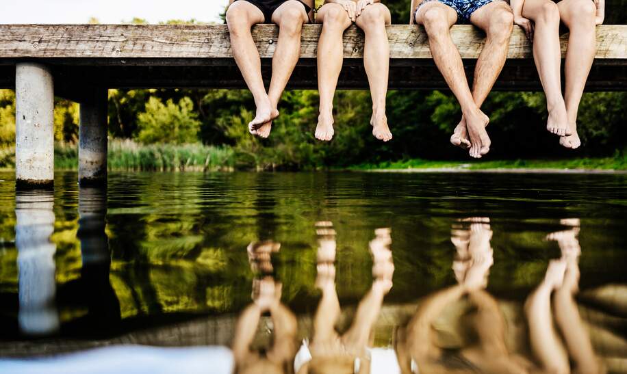 Gruppe von Freunden baumeln mit den  Beinen am Steg ueber dem See | © Gettyimages.com/TommL