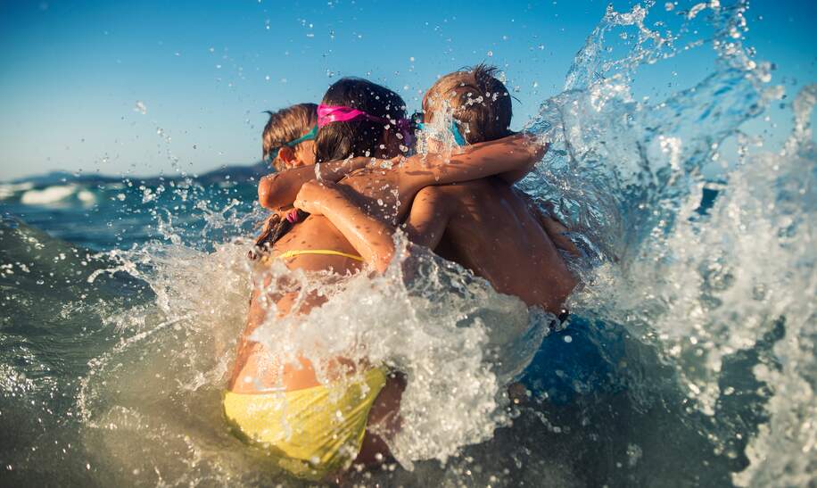 Kinder umarmen sich in den Meereswellen an einem sonnigen Sommertag | © Gettyimages.com/Imgorthand