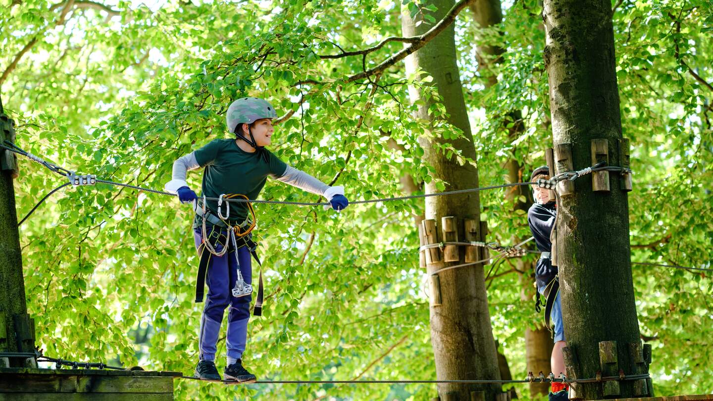 Junge mit Helm klettert auf einer Station im Hochseilgarten | © Gettyimages.com/romrodinka