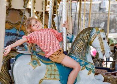 Laechelndes Maedchen auf einem Pferd eines alten Vintage-Karussells in Frankreich | © Gettyimages.com/romrodinka