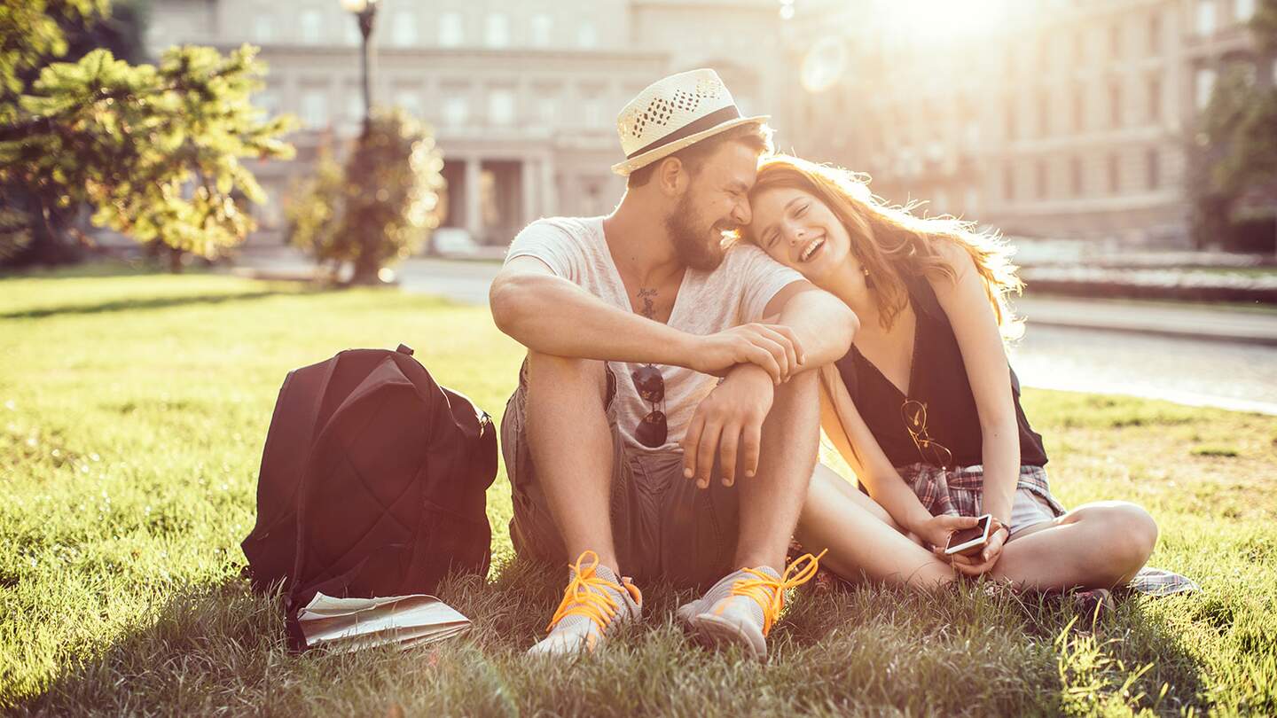 Junges Touristenpaar, das eine fremde Stadt erkundet. Im Park auf Gras sitzen und die Karte auf dem Smartphone ueberpruefen. Tragen Sie Freizeitkleidung und Rucksaecke. Genießen Sie den schoenen sonnigen Tag. | © Gettyimages.com/svetikd