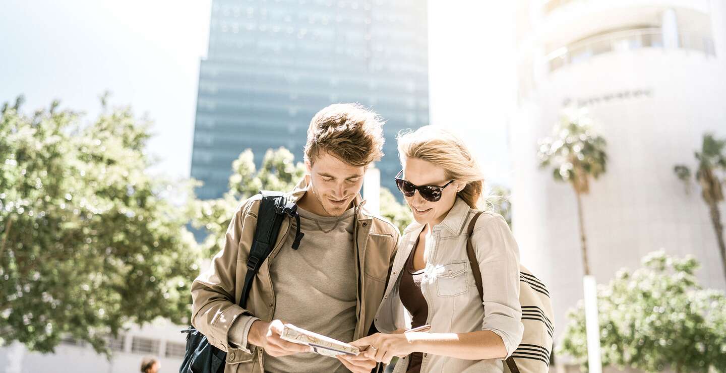 Ein Foto von einem Paar, das an sonnigen Tagen in der Stadt eine Karte liest. Glueckliche Touristen, die vor Gebaeude stehen | ©  Gettyimages.com/tommL