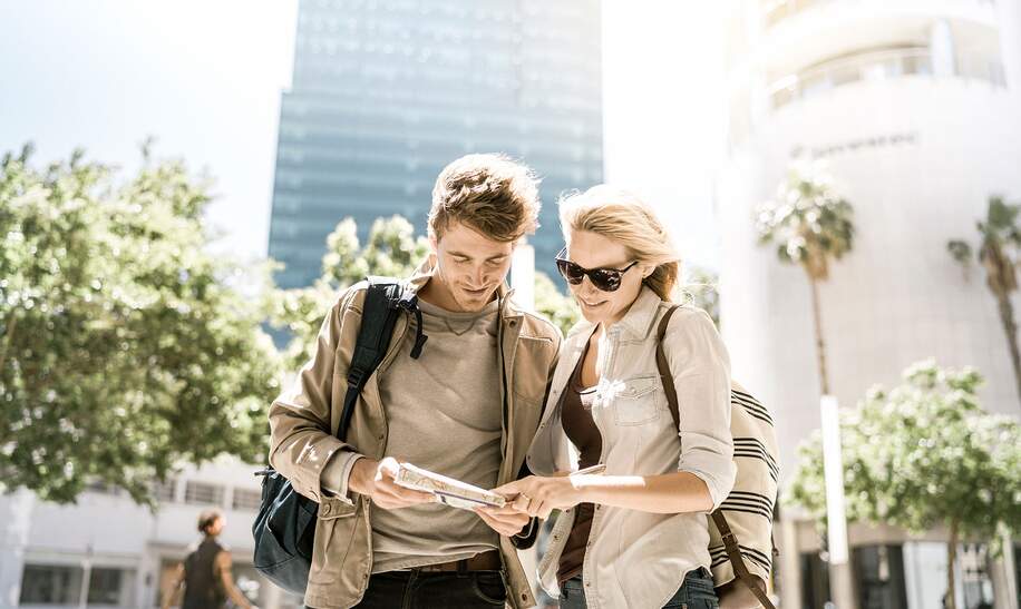 Ein Foto von einem Paar, das an sonnigen Tagen in der Stadt eine Karte liest. Glueckliche Touristen, die vor Gebaeude stehen | ©  Gettyimages.com/tommL