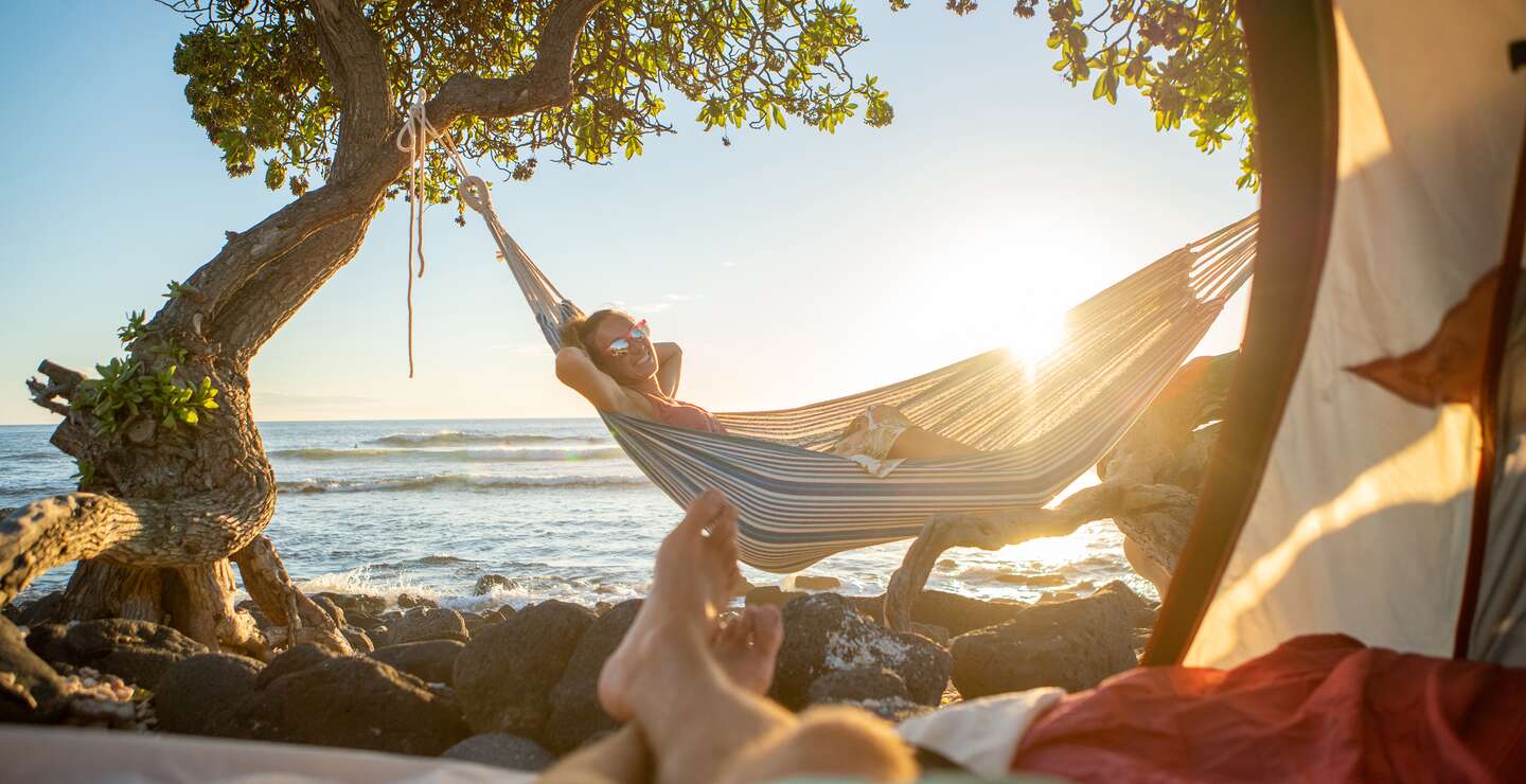 Paar am Strand, Mann blickt auf seine Freundin in der Haengematte | © Gettyimages.com/swissmediavision