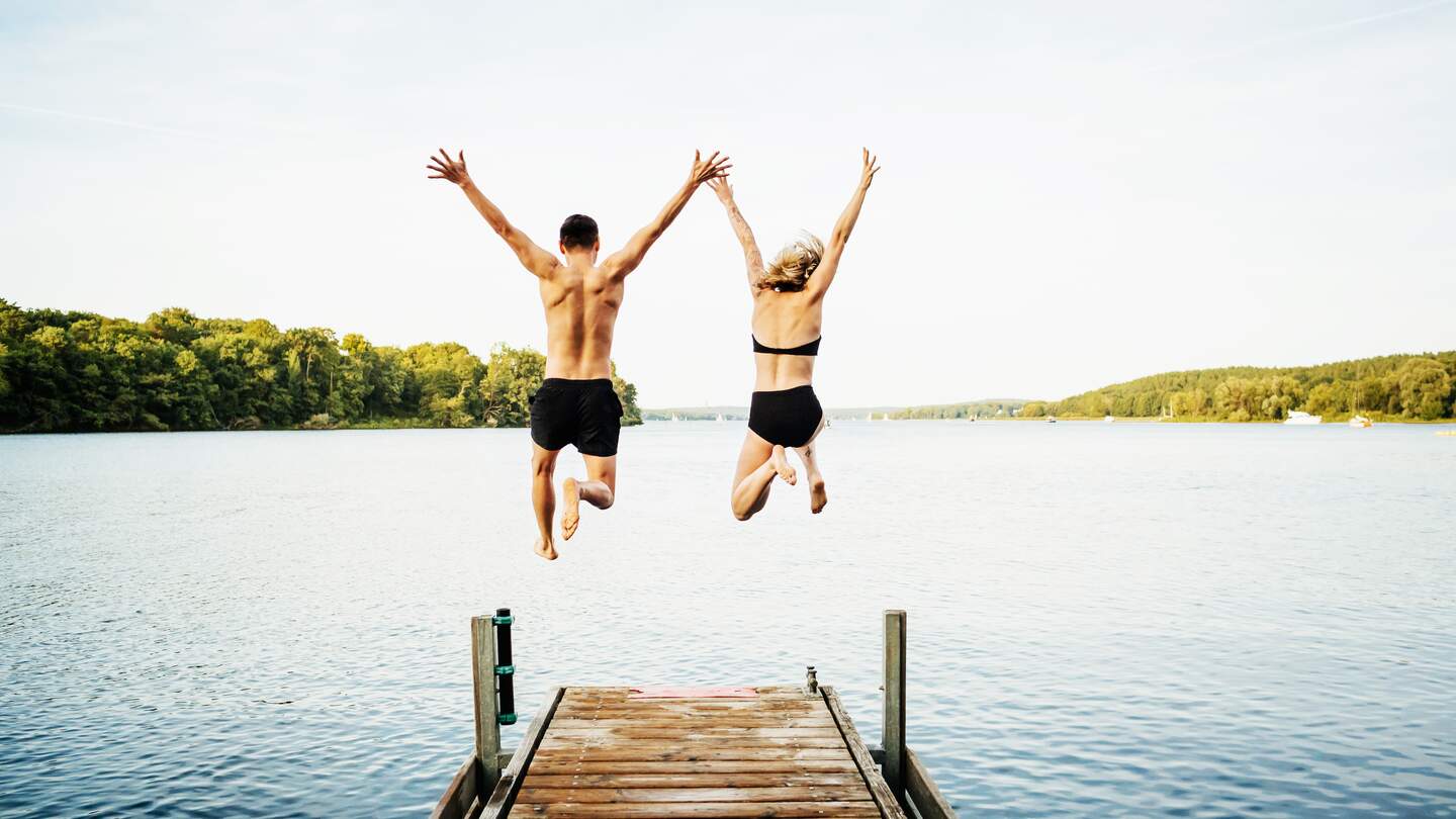 Rückenansicht eines jungen Paares, dass von einem Badesteg in einen See springt | © GettyImages.com/Franziska und Tom Werner