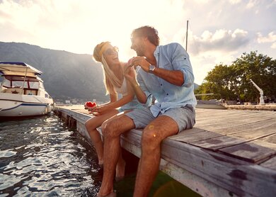 Glueckliches Paar, das Wassermelone isst und auf einem Holzsteg am Wasser sitzt | © Gettyimages.com/LuckyBusiness