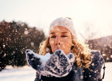 Frau im Freien im Winter pustet Schnee in die Luft | © Gettyimages.com/vgajic