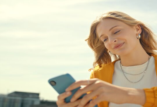 Frau sitzt auf einer Dachterrasse und schaut auf ihr Handy | © Gettyimages.com/marcovdm