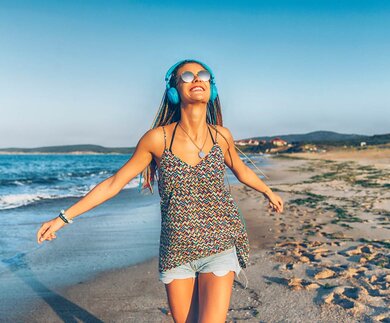 Froehliche junge Frau mit blauen Kopfhoerern, die am Strand Musik hört | © Gettyimages.com/Vladimir Vladimirov