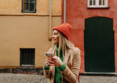Foto einer jungen Frau, die die Karten-App auf ihrem Handy verwendet, waehrend sie unterwegs ist und nach der richtigen Richtung sucht | © Gettyimages.com/AleksandarNakic