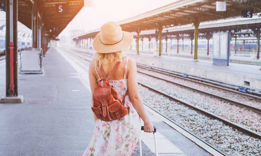 Junge Frau mit Rucksack im Sommer auf einenZug am Bahnhof wartend. | © GettyImages/Anna Berkut