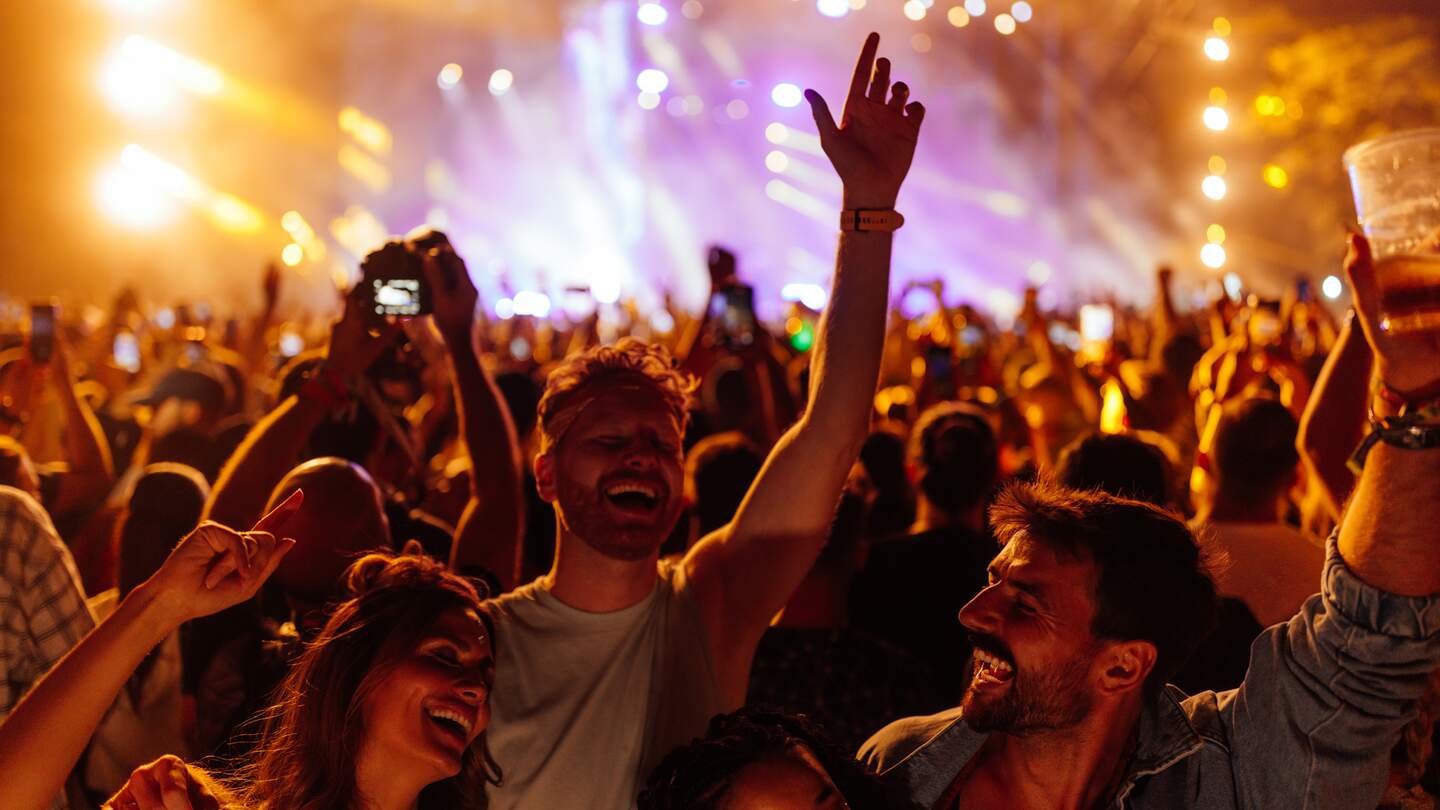 Eine Gruppe junger Freunde feiert auf einem Sommermusikfestival. Sie tanzen vor der Bühne.  | © Gettyimages.com/bernardbodo