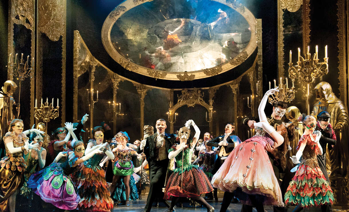 Ensemble des Musicals Das Phantom der Oper in aufwendigen Kostümen und Masken während einer großen Maskenball-Szene vor prunkvoller Bühnenkulisse. | © ATG ENTERTAINMENT GmbH/ UK Tour