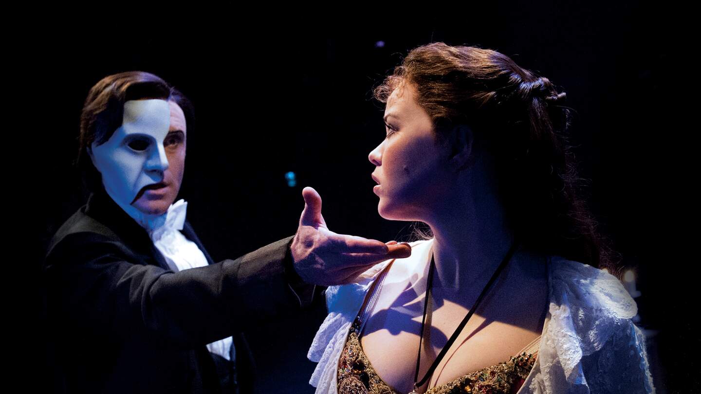 Das Phantom hält seine Hand an das Kinn von Christine. Dramatische Beleuchtung vor dunklem Bühnenhintergrund. | © ATG ENTERTAINMENT GmbH