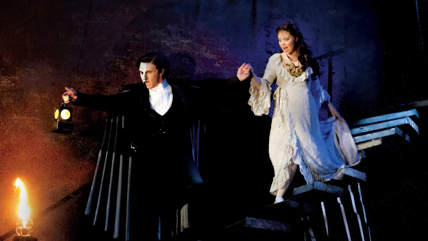 Das Phantom und Christine gehen eine Treppe hinab. Das Phantom hält eine leuchtende Laterne, Nebel und dunkle Beleuchtung prägen die Szene. | © ATG ENTERTAINMENT GmbH/Alastair Muir, UK Tour