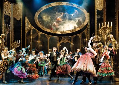 Ensemble des Musicals Das Phantom der Oper in aufwendigen Kostümen und Masken während einer großen Maskenball-Szene vor prunkvoller Bühnenkulisse. | © ATG ENTERTAINMENT GmbH/ UK Tour