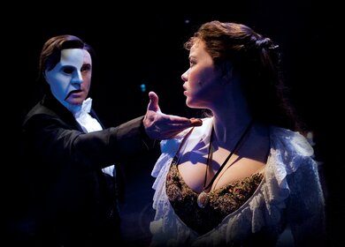 Das Phantom hält seine Hand an das Kinn von Christine. Dramatische Beleuchtung vor dunklem Bühnenhintergrund. | © ATG ENTERTAINMENT GmbH