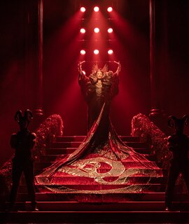 Frau steht in einem rotem Kleid mit  langer Schleppe auf einer roten Treppe | © Stage Entertainement, Matt Crockett