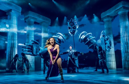 Meg von Disneys Hercules singend auf der Buehne, Hades mit spektakulaerem Buehnenbild im Hintergrund | © Stage Entertainment/Johan Persson 
