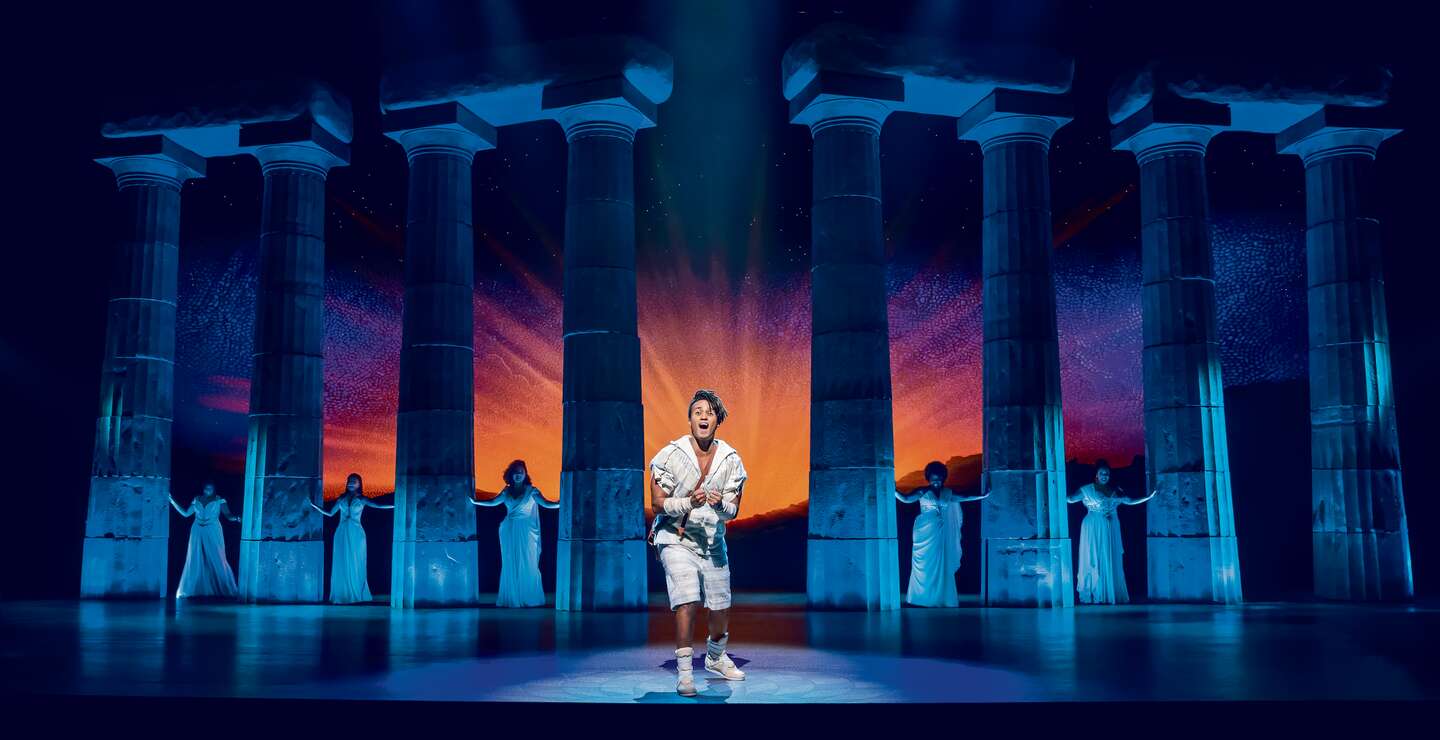 Disneys Hercules singt im Vordergrund, im Hintergrund sind Saenger in weissen Kleidern.  | © Stage Entertainment/Johan Persson 