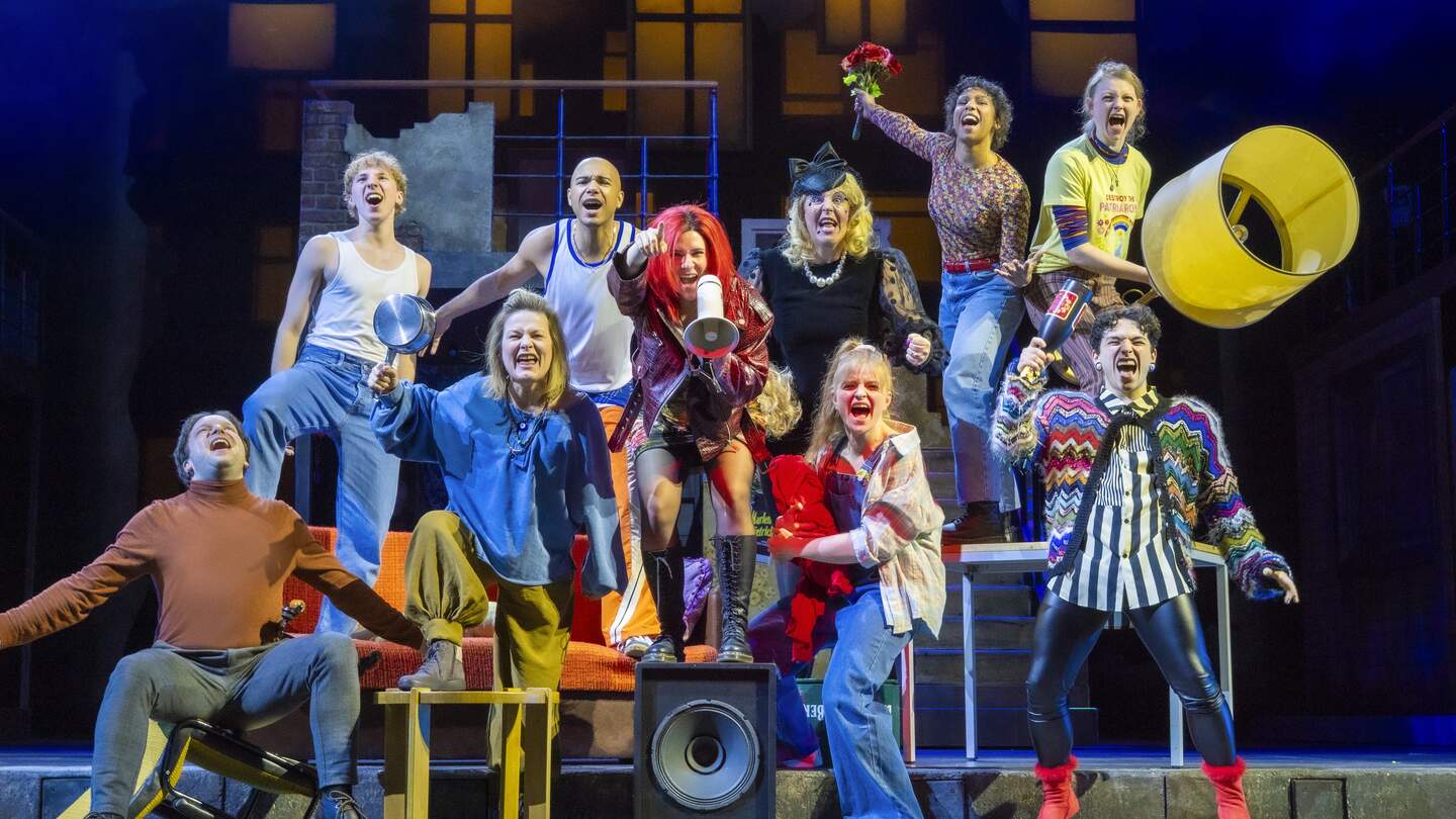 Ensemble auf der Bühne singt und jubelt, zentrale Figur mit Megafon im Mittelpunkt einer lebendigen Musicalszene aus wir sind am Leben. | © Stage Entertainement, Joern Hartmann