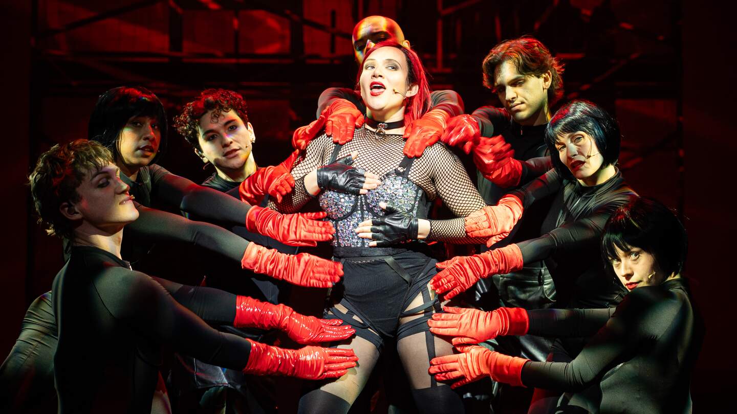 Musicalszene aus Wir sind am Leben: Zentrale Darstellerin im Fokus im roten Bühnenlicht. | © Stage Entertainement, Fokus Darstellerin