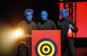 Blue Man Group hinter einer Zielscheibe, einer haelt einen Ballon in der Hand | © Stage Entertainment/Morris Mac Matzen