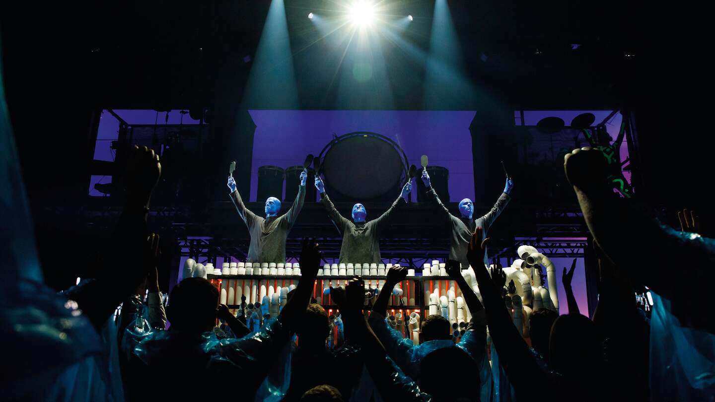 Die Blue man Group steht mit erhobenden Armen vor ihrem Publikium | © Stage Entertainment/Morris Mac Matzen