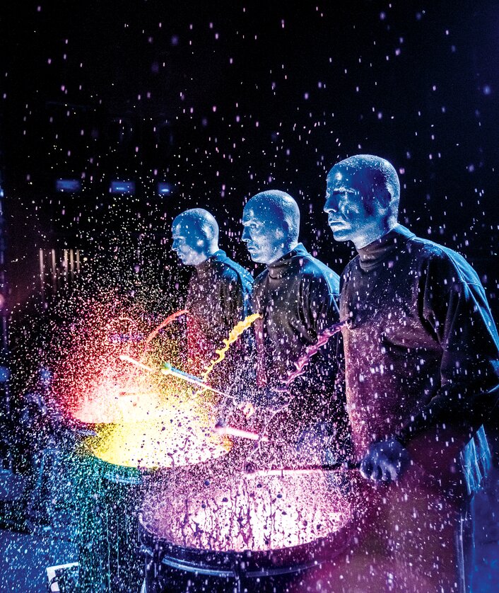Die Blue Man Group spielt auf Farbtrommeln, gelbe und pinke Farbe spritzt durch die Luft | © Stage Entertainment