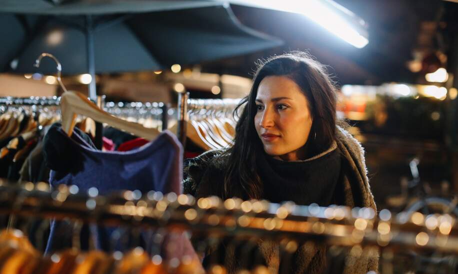 Frau schaut Kleidung an auf einem Berliner Flohmarkt bei Nacht. | © Gettyimages.com/lechatnoir