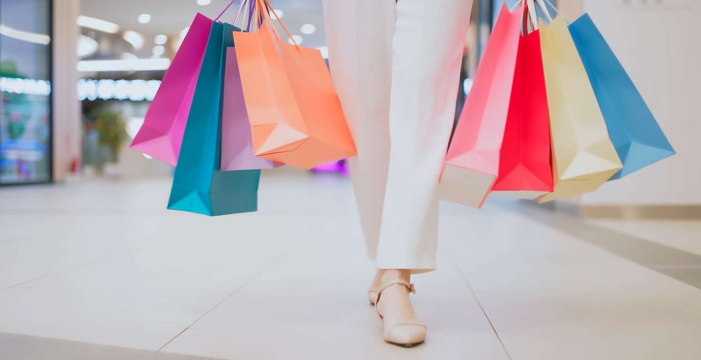 Frau trägt bunte Einkaufstüten und käuft durch ein Einkaufszentrum.  | © Gettyimages.com/