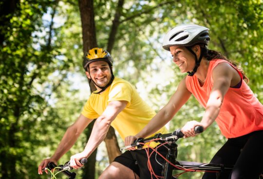 Das junge Paar faehrt im Sommer mit kurzer Kleidung auf einem Weg mit Baeumen | © GettyImages.com/microgen