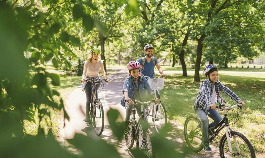 Mutter, Vater, und zwei Kinder fahren im Wald Fahrrad und tragen alle Fahrradhelme. | © Gettyimages.com/vgajic Miodrag Gajic