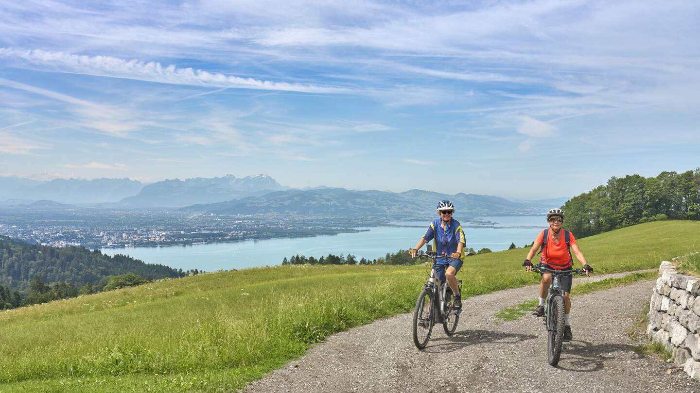 Zwei Radfahrer auf einem Höhenweg am Bodensee mit Blick auf See und Berge. | © GettyImages.com/	Uwe Moser
