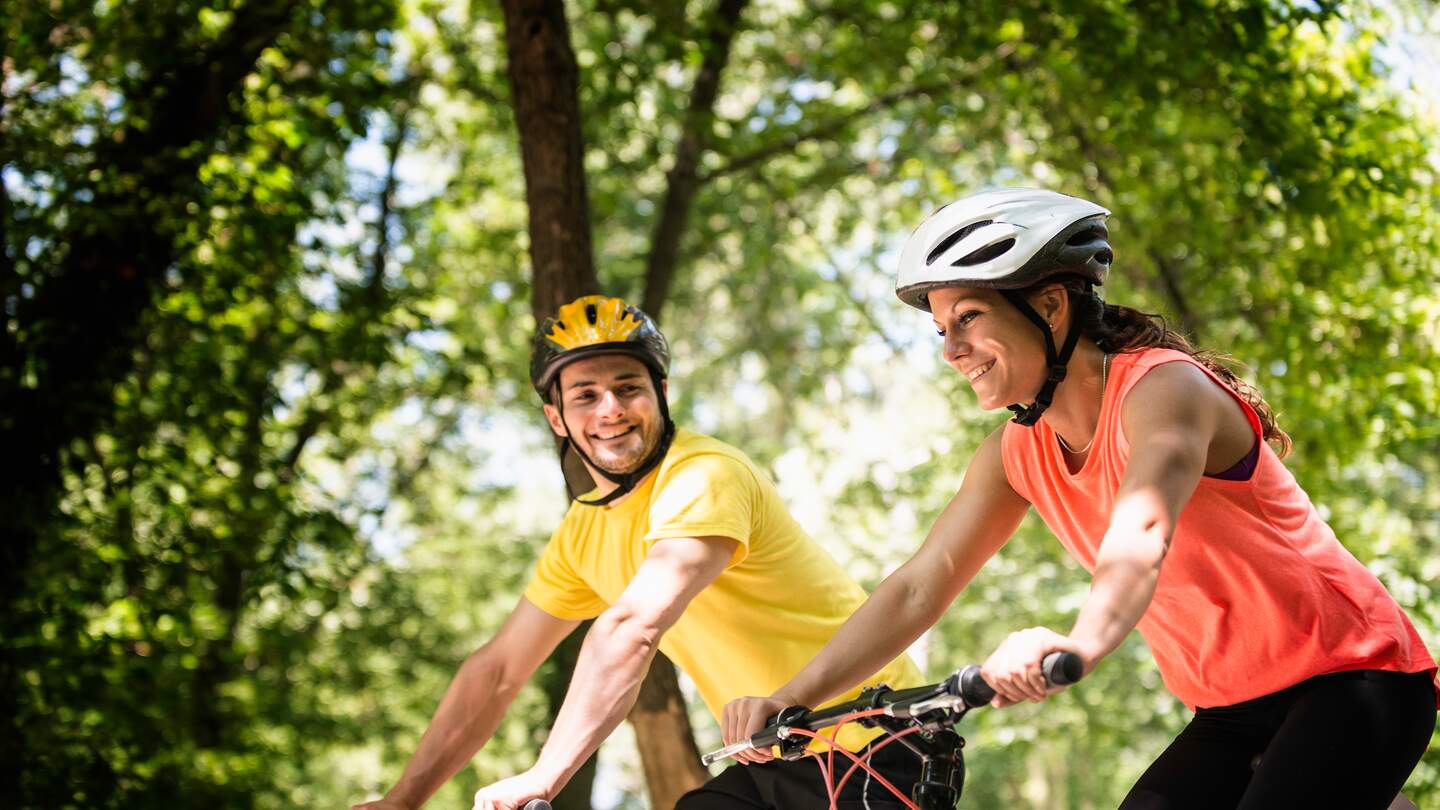 Das junge Paar faehrt im Sommer mit kurzer Kleidung auf einem Weg mit Baeumen | © GettyImages.com/microgen