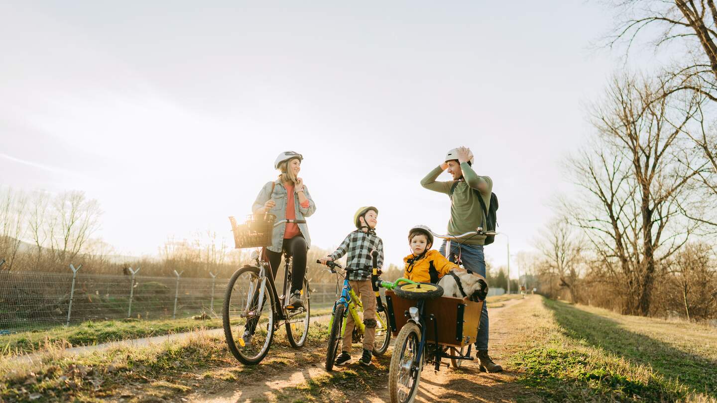 Junge Familie mit zwei Kindern, die an einem sonnigen Frühlingstag gemeinsam mit ihrem Haustier eine Radtour unternimmt | © GettyImages.com/AleksandarNakic
