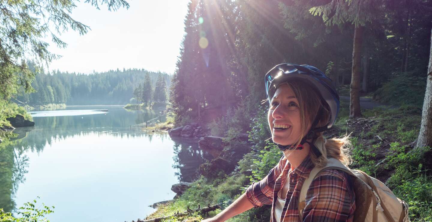 Frau auf dem Mountainbike mit Blick auf schönen Alpensee mit Sonnenschein | © GettyImages.com/Mystockimages