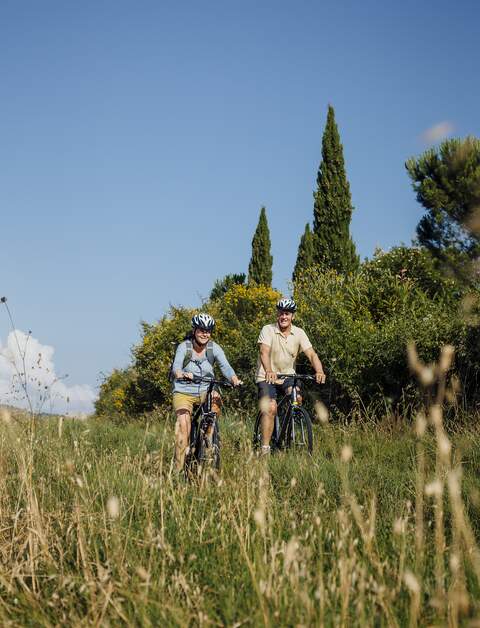Seniorenpaar faehrt mit Mountainbikes bei gutem Wetter ueber ein Feld bei blauem Himmel | © Gettyimage/SolStock